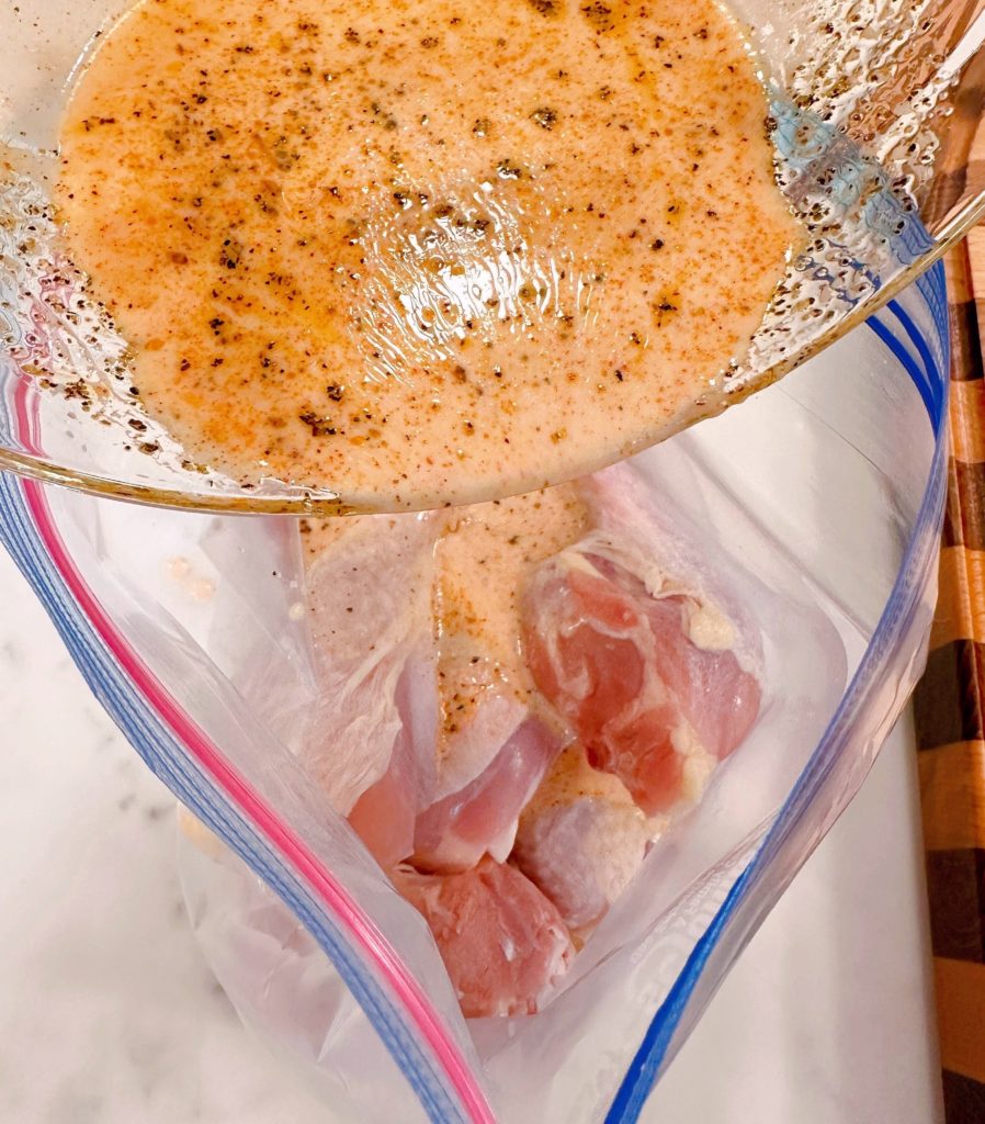 Chicken in a resealable plastic bag with marinade being poured over it.