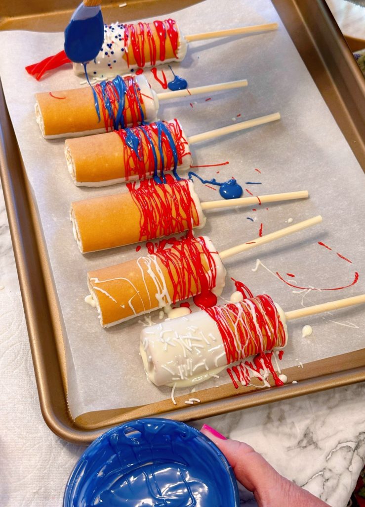 Cake pops on a parchment lined baking sheet with red chocolate drizzled across the bottom of each cake pop.