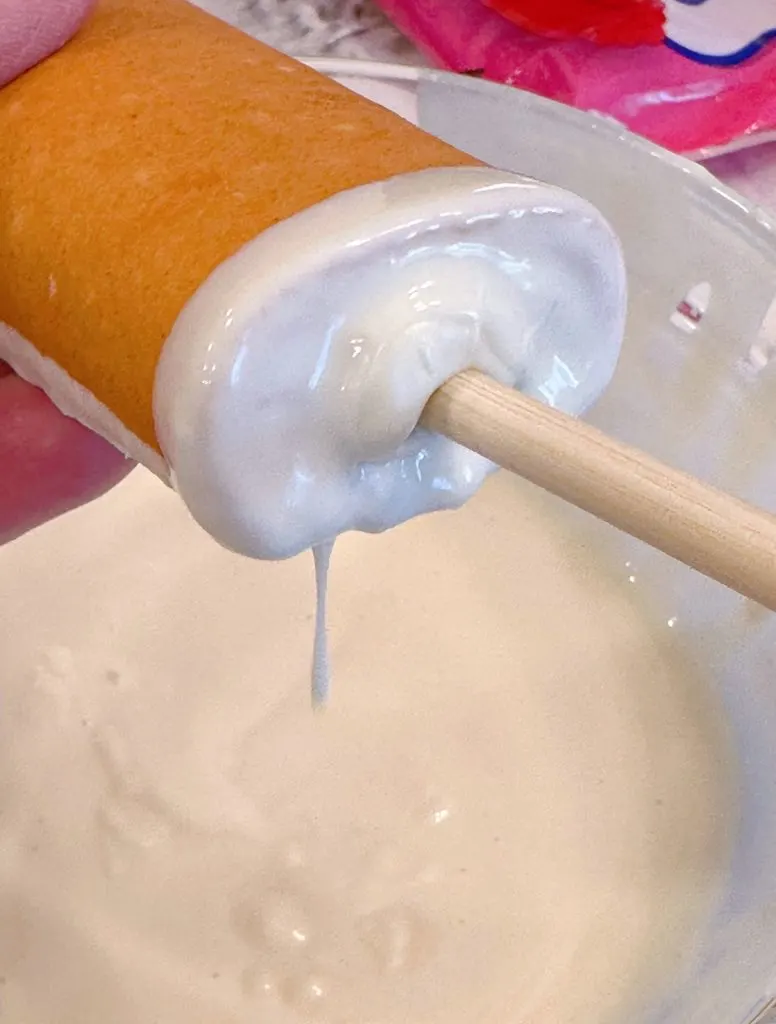 Inserting a treat stick into the bottom of each cake roll.