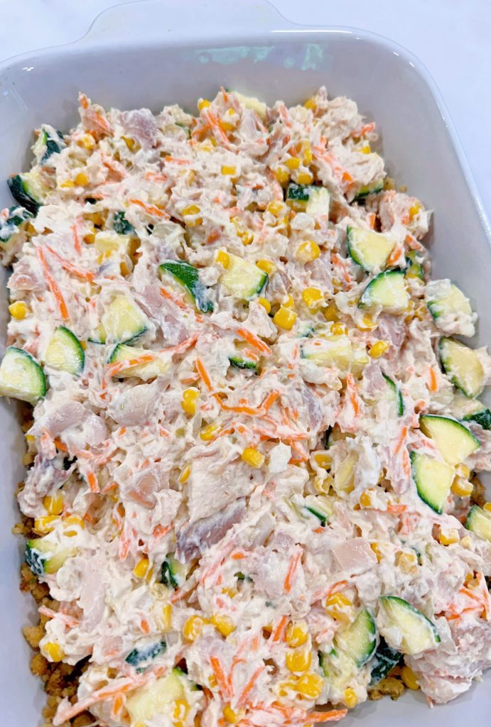 Chicken zucchini filling is poured over the stuffing mixture in the casserole dish.