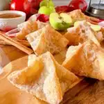 Fried Apple Pie bites rolled in cinnamon sugar on a wood cutting board with apples and cinnamon sticks.