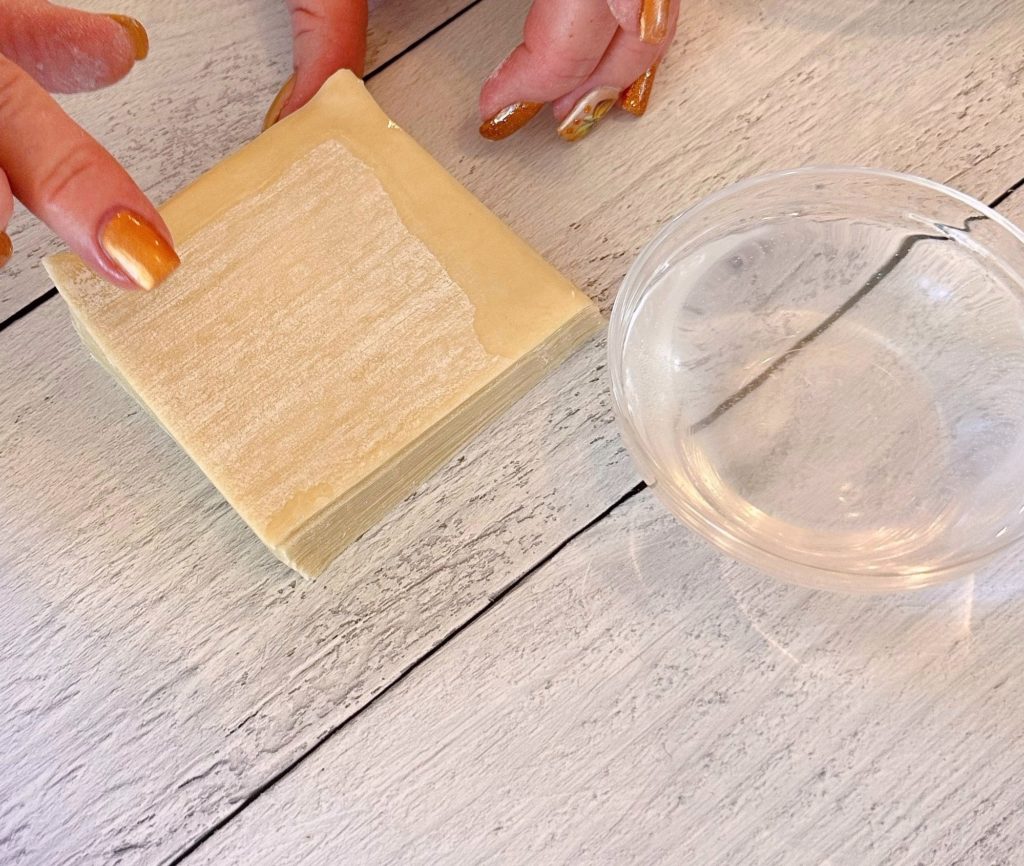 Wonton wrappers on flat work surface with a small bowl of water.