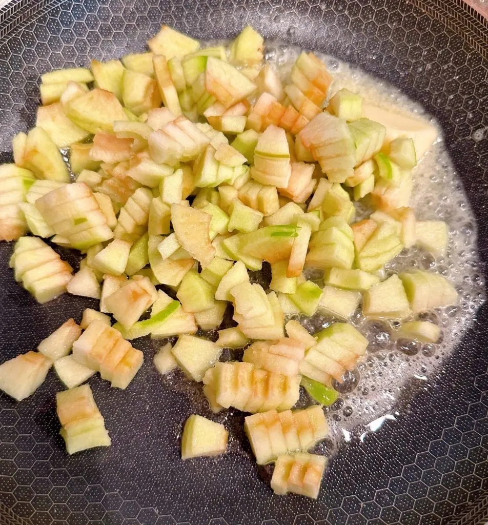 Apple sauting in melted butter in skillet.