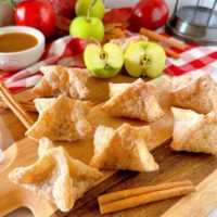 Apple Pie Bites on a wooden cutting board with apples, caramel, and cinnamon sticks.