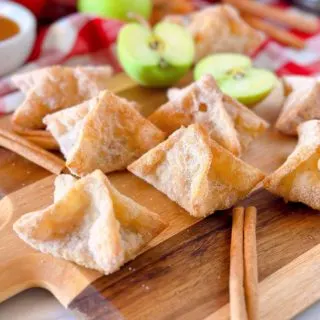 Apple Pie Wonton Bites on a wooden cutting board with apples and cinnamon sticks.