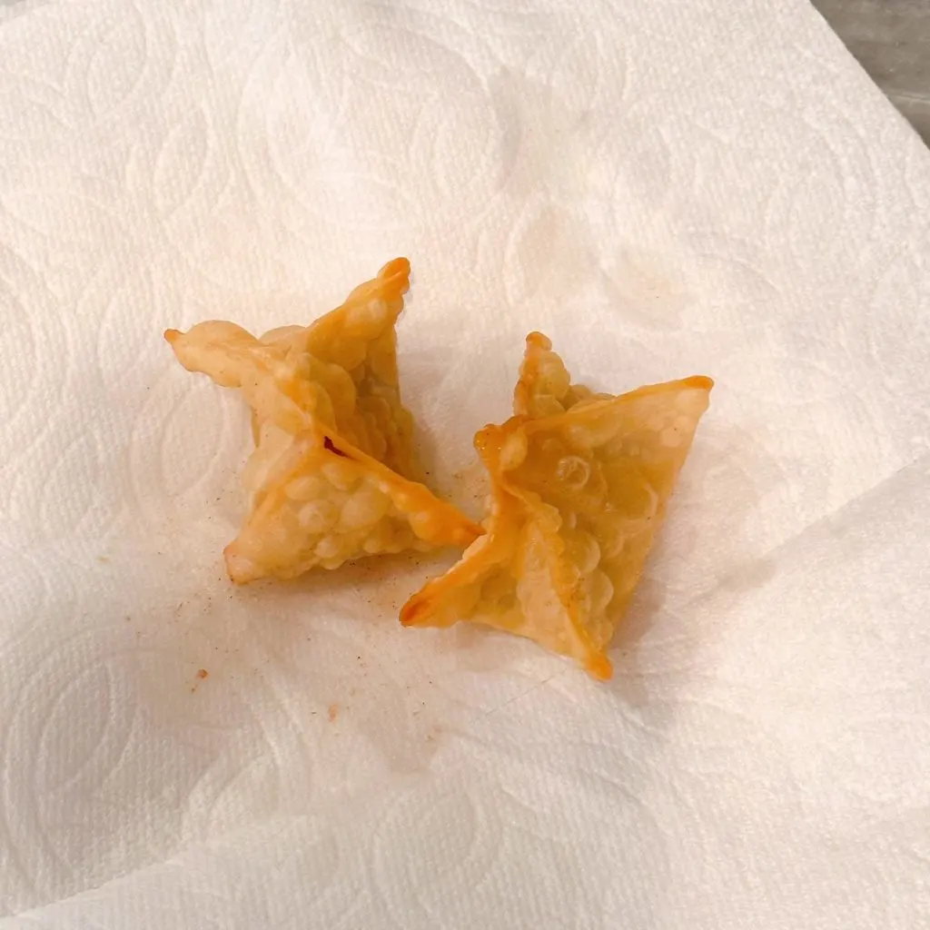 Placing fried apple pie bites on a paper towel lined plate.