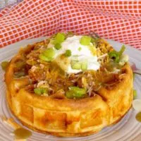 Cornbread waffle stuffed with chili and cheese and topped with sour cream and more cheese on a dinner plate.