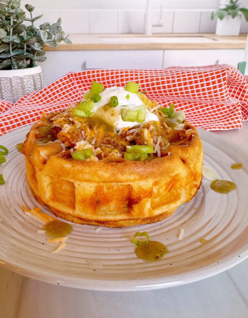 Stuffed Cornbread waffle with chili and cheese. Topped with sour cream, chives, and hot sauce.