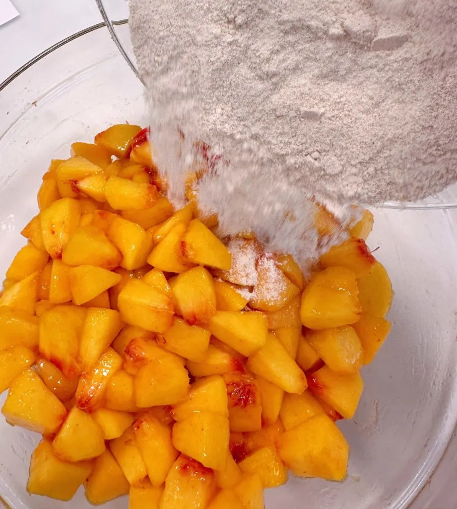 Pouring dry ingredients over the peaches.