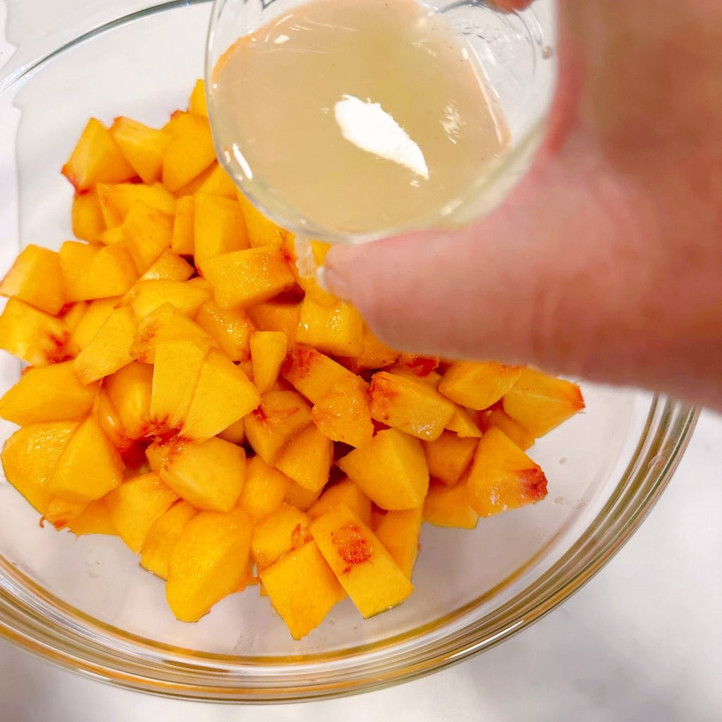 Peaches in a large bowl with lemon juice being sprinkled over the top of them.