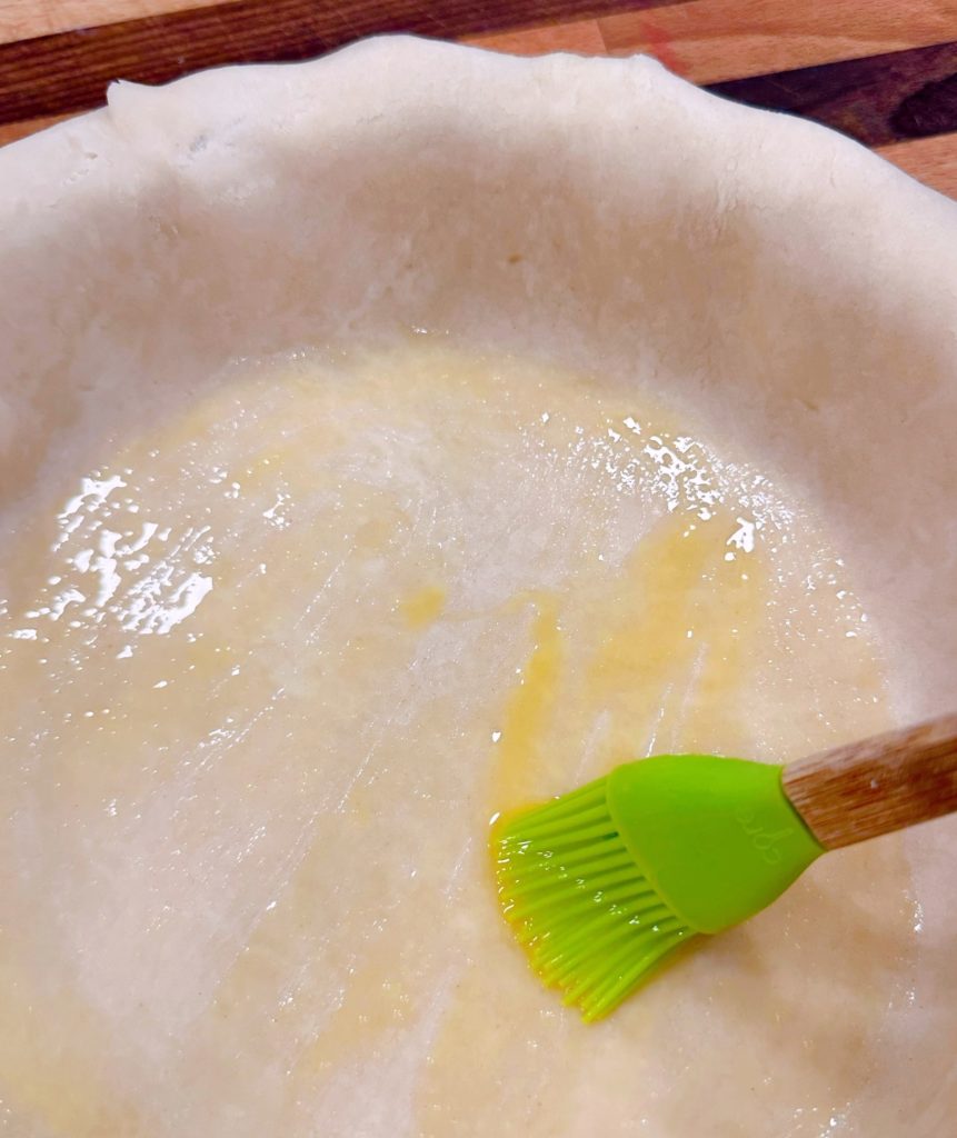 Lining the bottom crust in the pie plate and brushing it with egg wash.