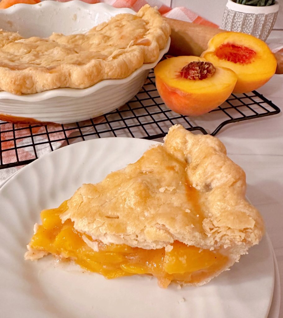 A fresh peach pie is sliced and served on a white dessert plate.