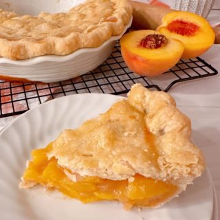 A fresh peach pie is sliced and served on a white dessert plate.