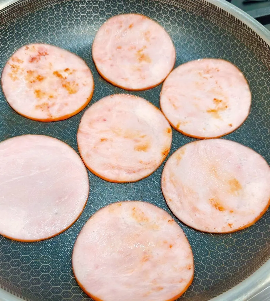 Browning and warming the canadian bacon in a large skillet over the stove.