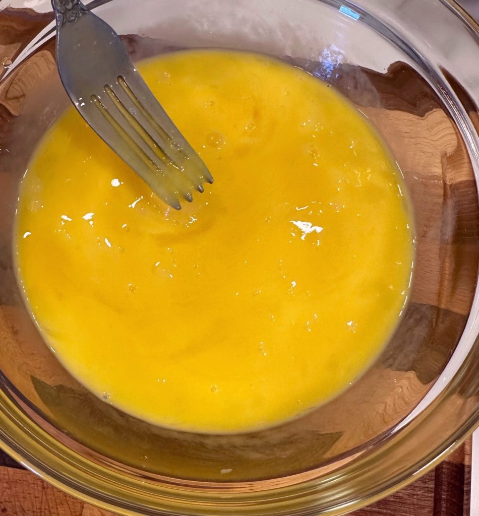 Whisking large eggs in a medium bowl.