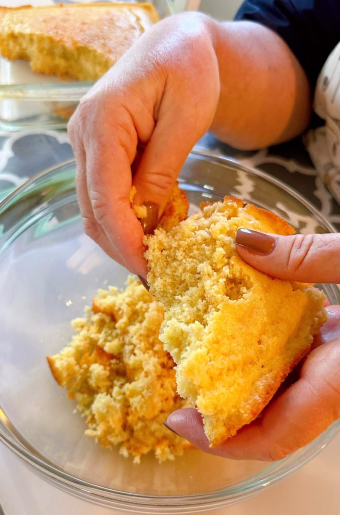 Crumbling cornbread in a large bowl.