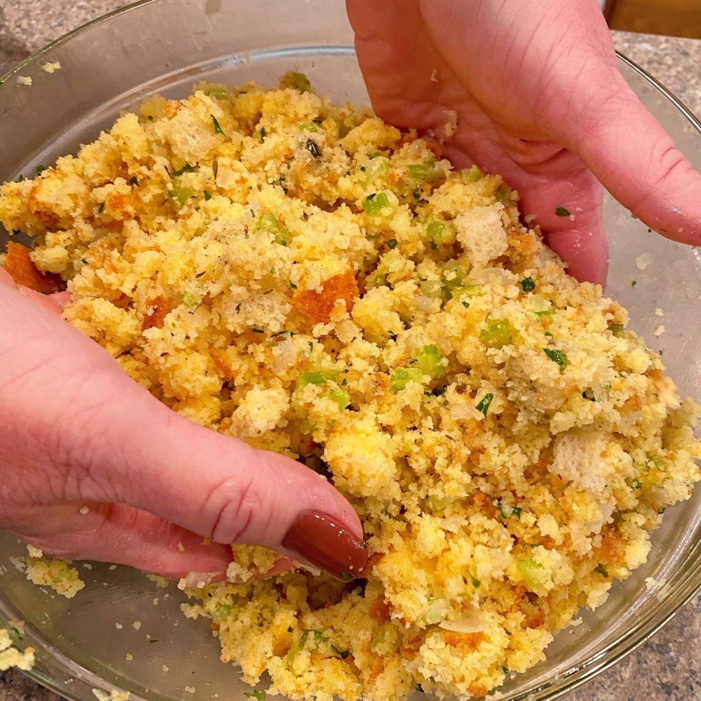 Mixing cornbread dressing with hands in a bowl.