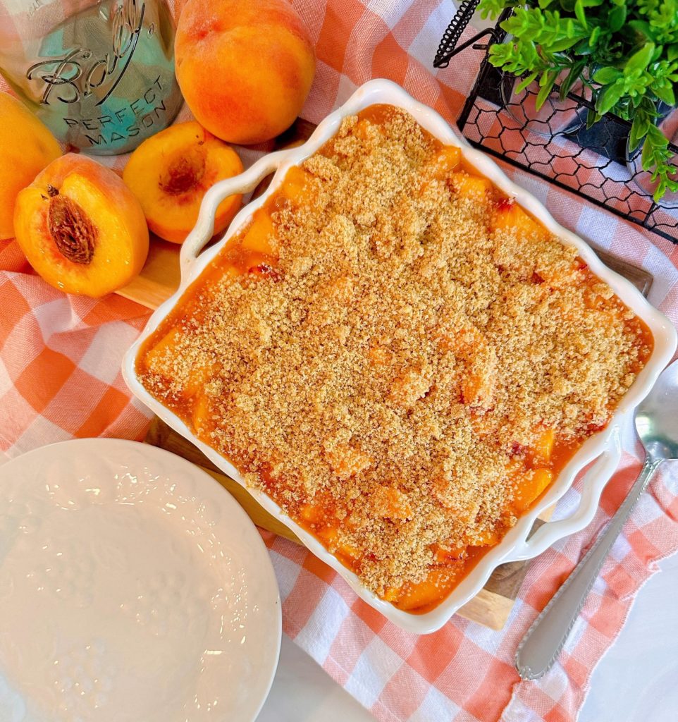 Layered Peach Delight Dessert in a white baking dish with peaches nestled around it.