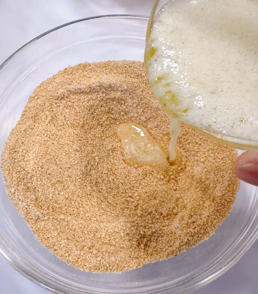 Adding butter to graham cracker mixture to create crust.