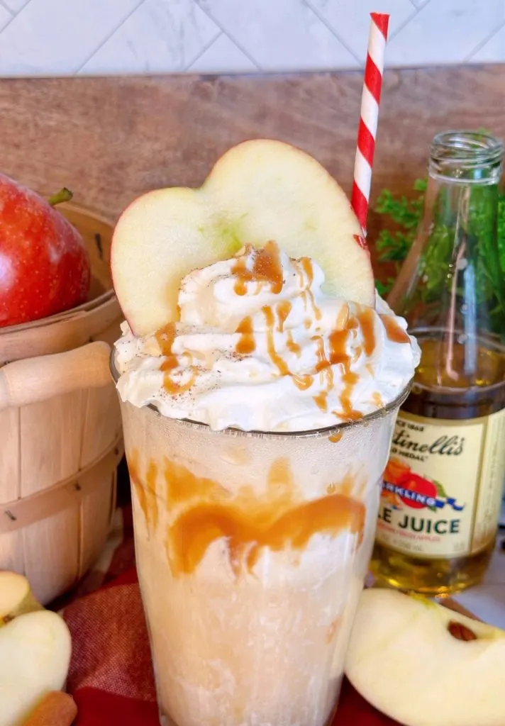 Apple cider float topped with whipped cream, a slice of fresh apple, and a drizzle of caramel.