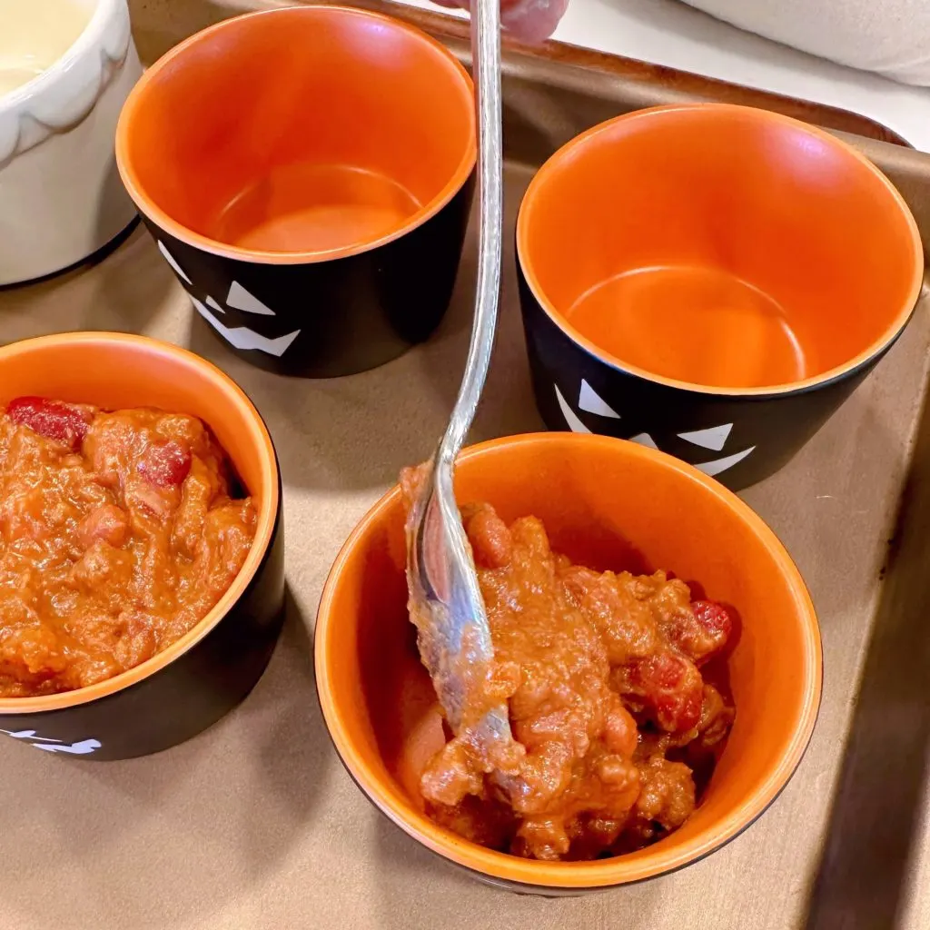 Filling each ramekin cup with canned chili.