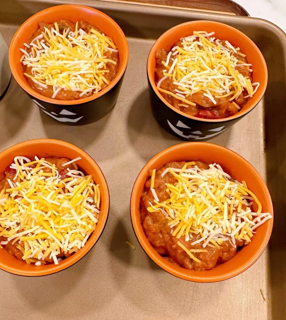 Each ramekin of chili is topped with grated cheese.