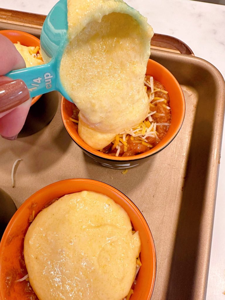 Pouring cornbread mix batter over the chili and cheese in the ramekin.