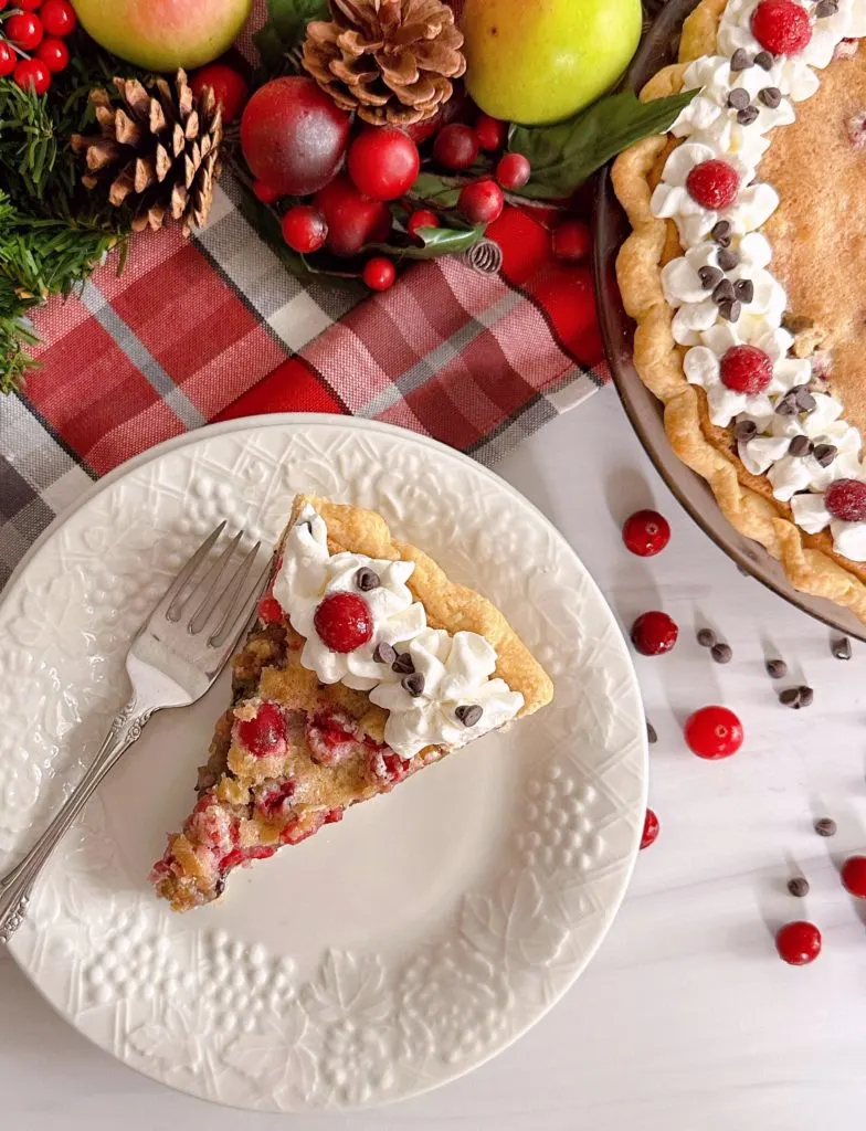 Slice of cranberry walnut chocolate chip pie on a plate with a full pie in the background.