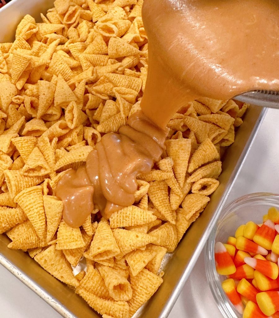 Pouring caramel-peanut butter sauce over bugles.