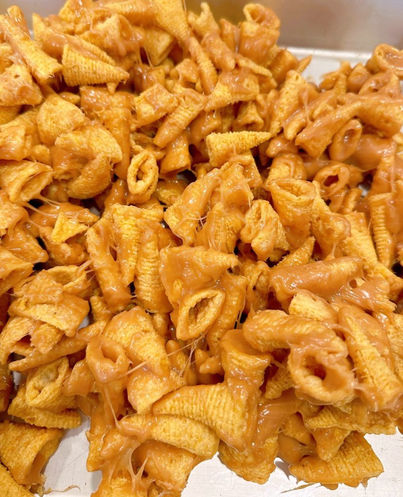 Caramel peanut butter covered bugles on a baking sheet.