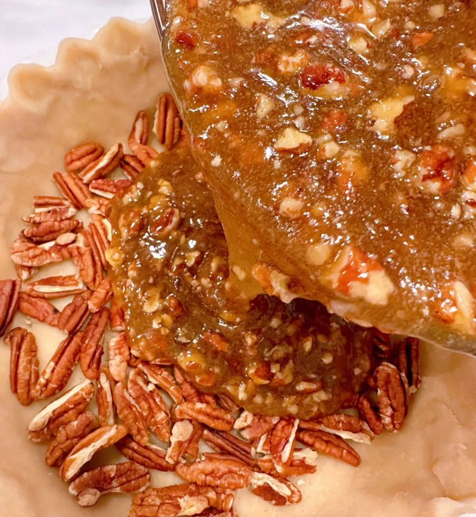 Pouring caramel pecan filling over quartered pecans in the pie crust.