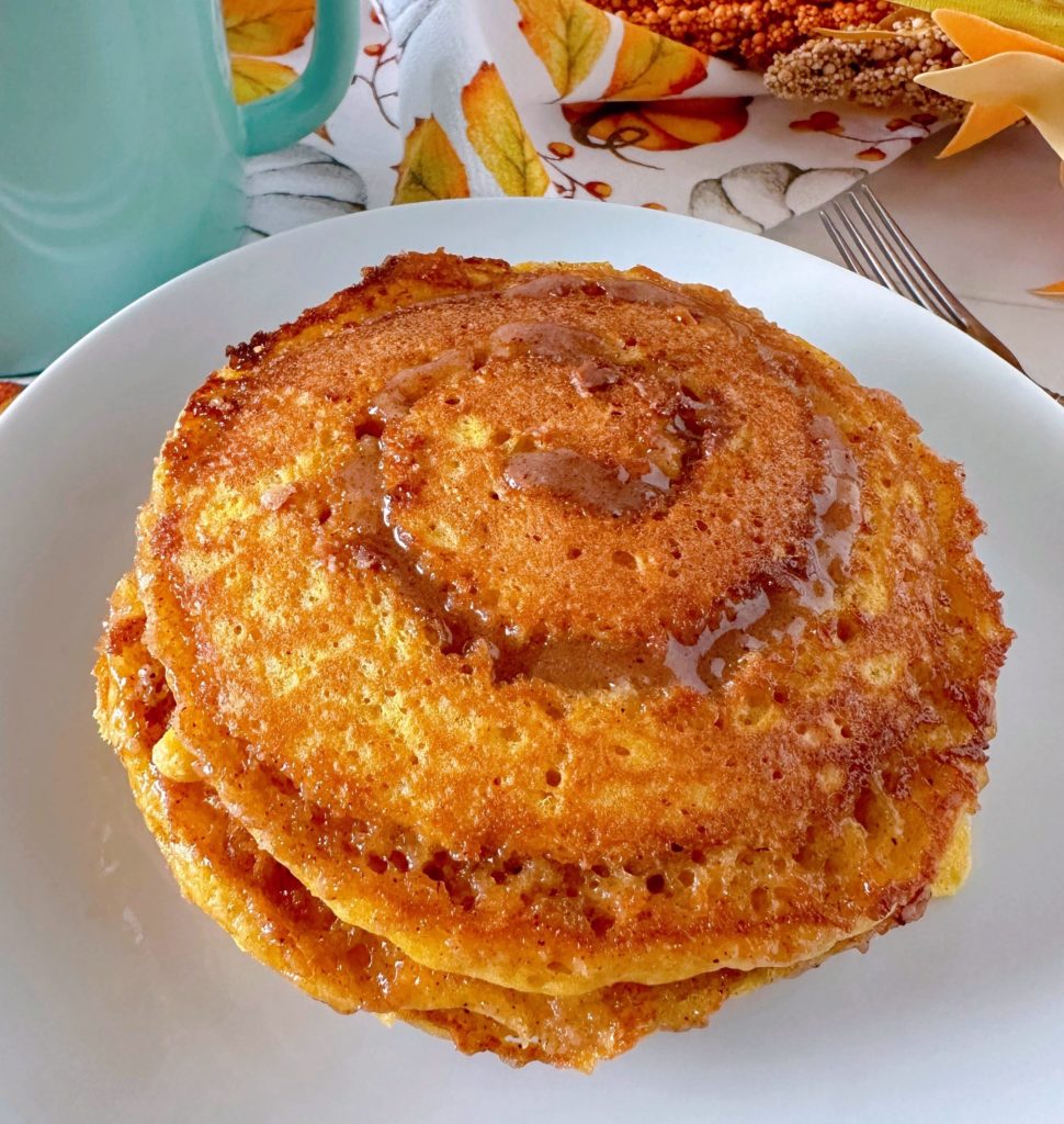 Pumpkin Spice Cinnamon Roll Pancakes in a stack on a white plate.