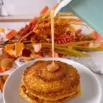 Pouring cinnamon bun syrup over the top of a stack of pumpkin cinnamon pancakes.