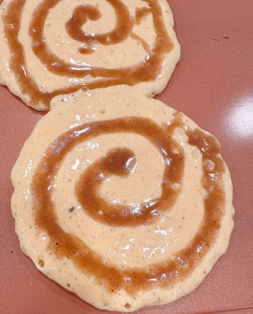 Cinnamon Pumpkin Pancakes cooking on the griddle with the cinnamon swirl on top.