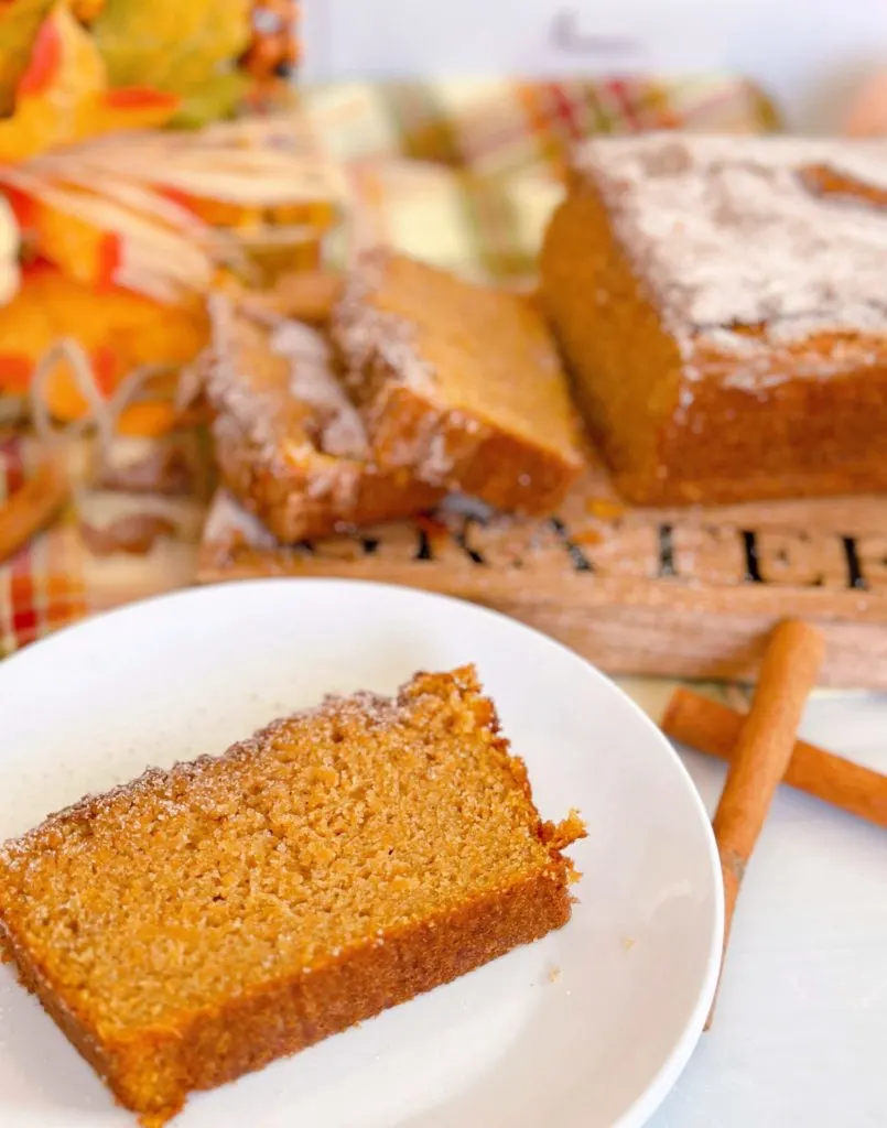 A slice of sweet potato bread on a white plate with the rest of the loaf in the background.