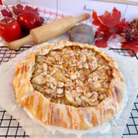 Apple Almon Galette on a cooling rack with a rolling pin and apples in the back ground.