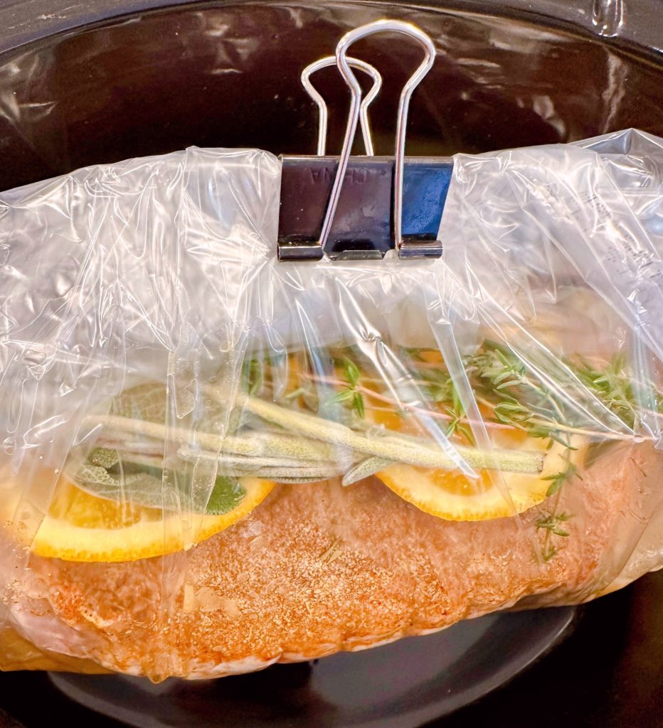 Enclosing turkey roast inside a slow cooker liner bag and clipping with metal clip.