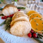 Slow Cooker Turkey Breast slice and on a platter with orange slices, herbs, and gravy.