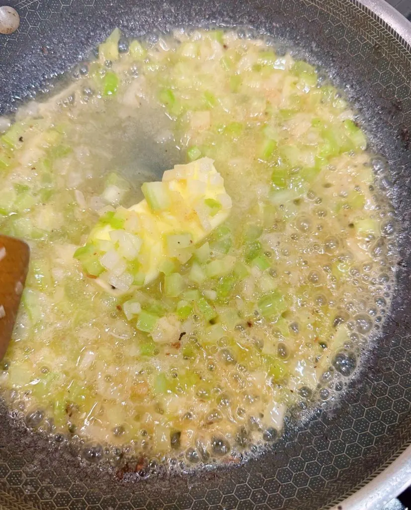 Cooking onions and celery in melted butter on the stove top.