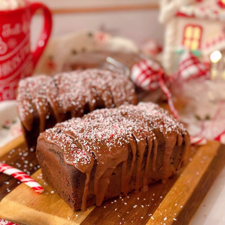 Two mini Chocolate Peppermint Loaf cakes on a mini cutting board with Christmas stuff in the background.