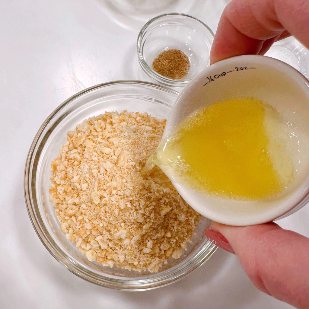 Adding melted butter to crushed cracker crumbs.