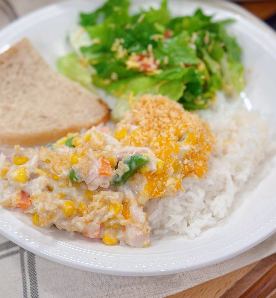 Amish Chicken Casserole over rice on a dinner plate with salad and a slice of bread.