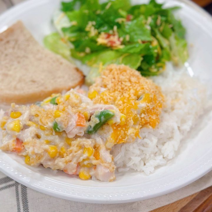 Amish Chicken Casserole over rice on a dinner plate with salad and a slice of bread.