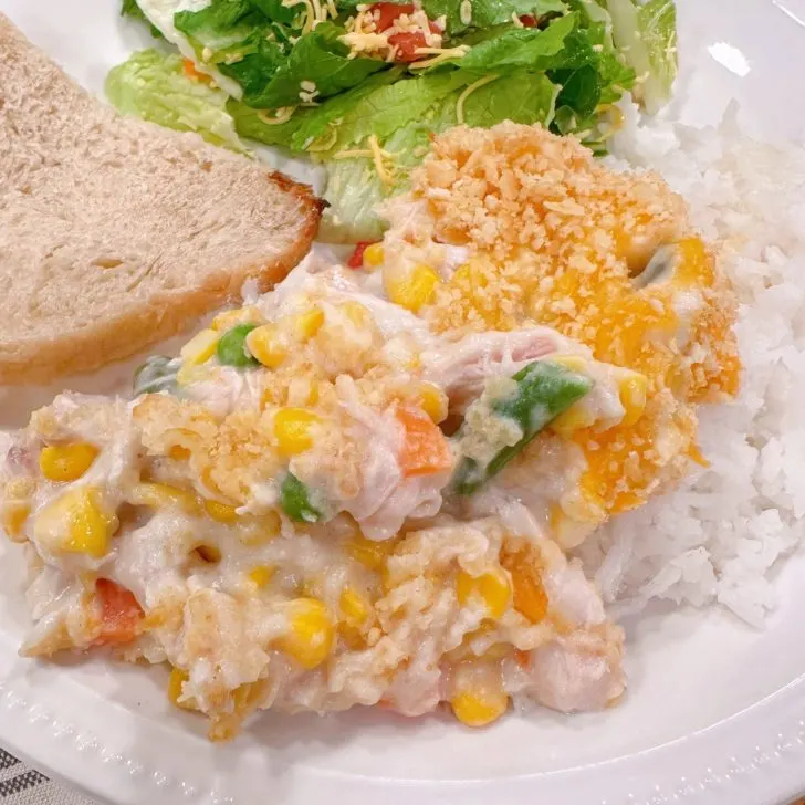 Amish Chicken and Corn casserole on a dinner plate with salad and crispy bread.