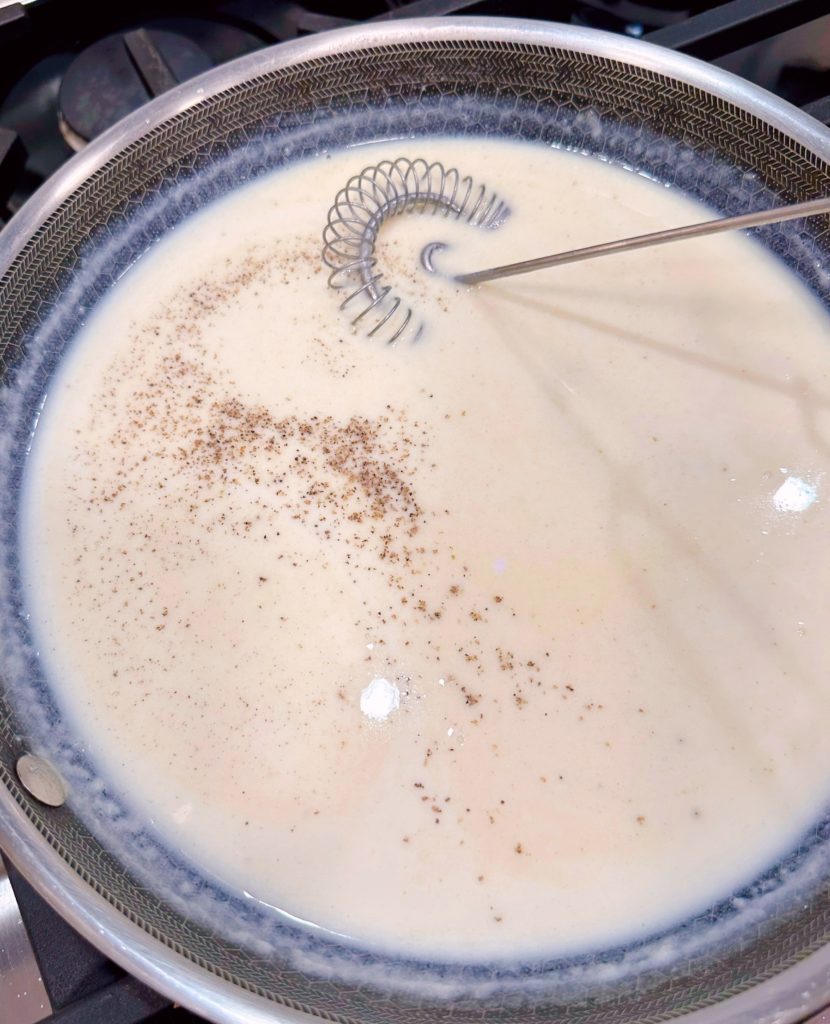 White cream sauce with seasonings on the stove top.