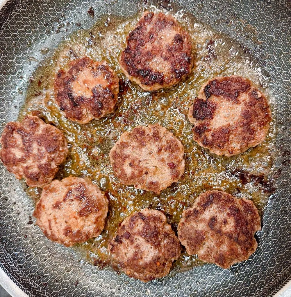 Hamburger patties cooking in the skillet.