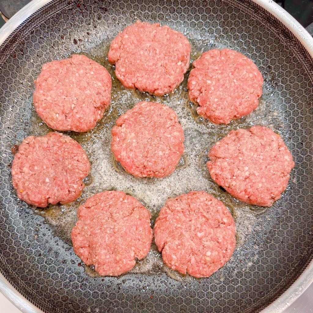 Cooking hamburger patties in a large skillet.