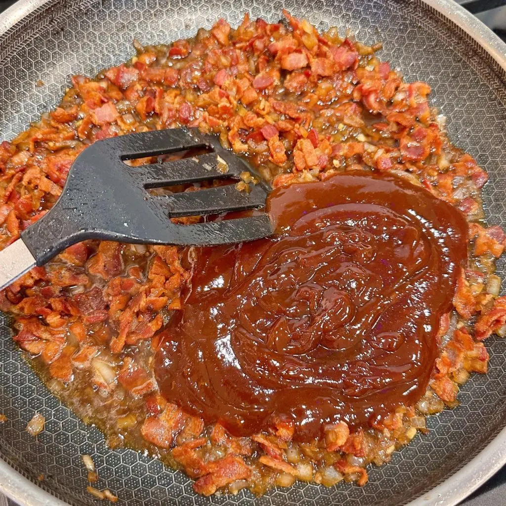 Adding BBQ sauce to bacon and whiskey mixture.