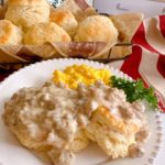 Sausage and biscuits with a basket of biscuits in the background.