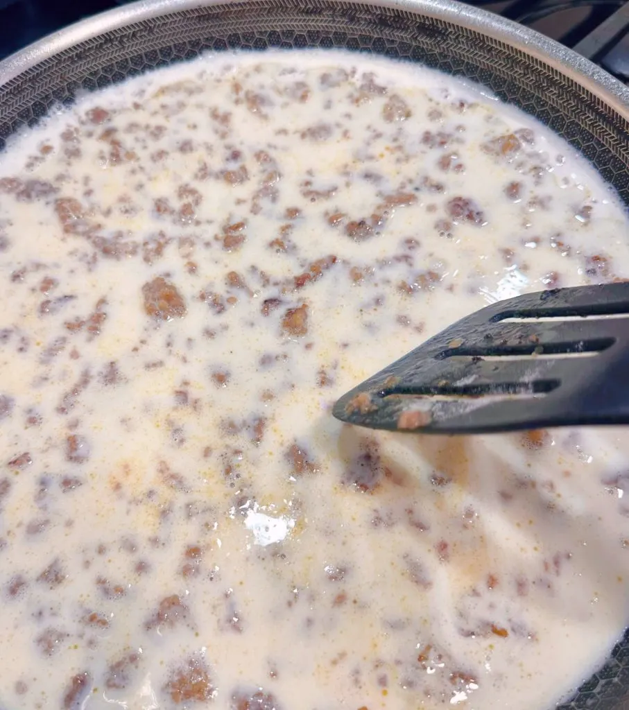 Stirring Milk and Sausage together in skillet.